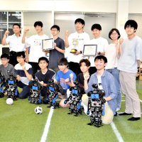 優勝メンバーの人型ロボ選手と学生たち。新習志野キャンパスの一角に、サッカーフィールドを再現した拠点がある
