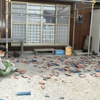 屋根から落下した瓦を片付ける釣り船店の女性＝１１日午前１０時２０分ごろ、木更津市
