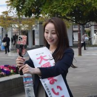 自撮り棒に取り付けたスマートフォンでライブ配信する大塚さん＝４月６日、ＪＲ海浜幕張駅前
