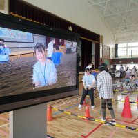 「ＡＲゴーグル」をつけて歩く児童（奥）が見ている映像を映し出しすモニター（左）＝鎌ケ谷市
