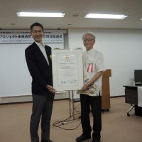 柏市役所で登録証を渡された萩原理事長（左）。右は活動の調査に当たった琉球大の土屋誠名誉教授＝１５日
