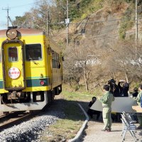 復旧工事が終わった被災現場で、運行を再開した列車に向かって手を振る関係者ら＝２５日午前、大多喜町庄司