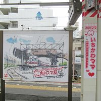 「いちかわママ」のホーム駅名看板。地元在住の画家が描いた同駅イラストも展示＝３０日、市川市
