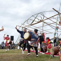１５０周年を記念して万国旗と大漁旗を飾った灯台の下でイベントを盛り上げる銚子はね太鼓保存会＝１６日、銚子市