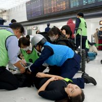 足に重傷を負った成田空港の旅客を演じる学生を救護する訓練参加者ら
