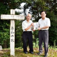平和の塔の脇で冊子「二度目の着地」を手にする東庄郷土史研究会の野口さん（右）と平野さん
