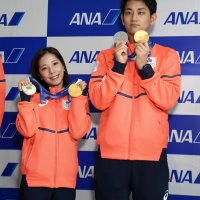 ミラノ・コルティナ冬季五輪で獲得した金と銀のメダルを成田空港で掲げるフィギュアスケートペアの（左から）三浦選手と木原選手＝２４日午後、成田市